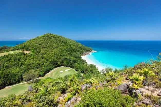 Stunning view of Anse Georgette with lush greenery, a pristine white beach, and turquoise ocean waters.