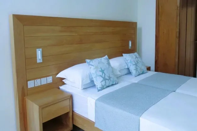 Bright bedroom at Lyla Beach Villa featuring a wooden headboard, white bedding, and ocean-inspired pillows, perfect for a relaxing beachside vacation.