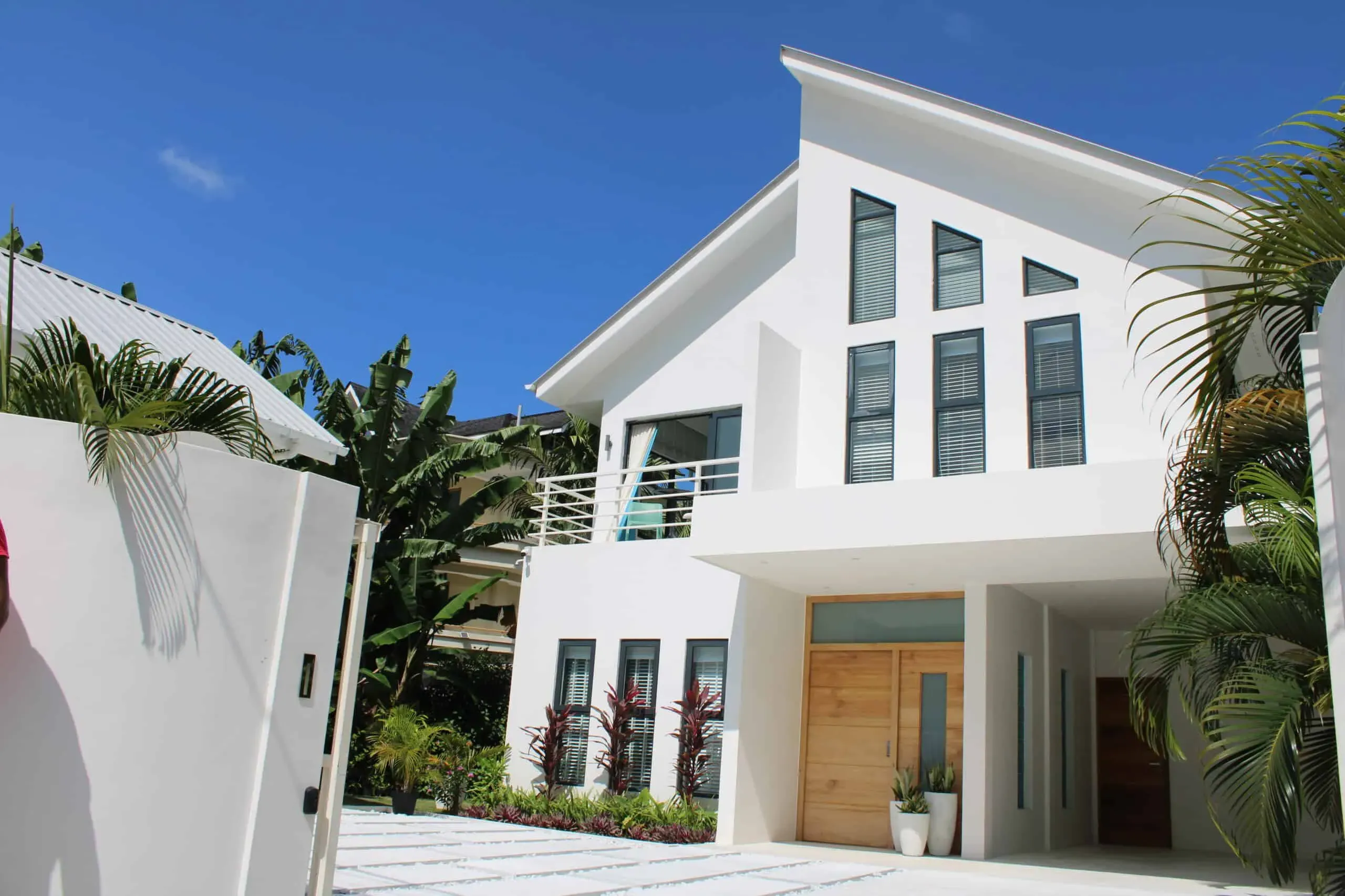 Modern white villa with large windows and tropical landscaping, offering luxury vacation rental near the beach. Perfect for a relaxing getaway in a contemporary coastal setting.
