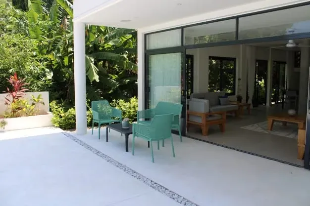 Modern villa outdoor patio with seating area and lush tropical gardens, ideal for relaxation at Lyla Beach Villa. Perfect for a luxurious beachside vacation experience.