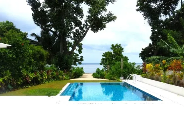 Lyla Beach Villa outdoor pool with lush tropical greenery and ocean view, perfect for relaxing vacation stays on the beach.