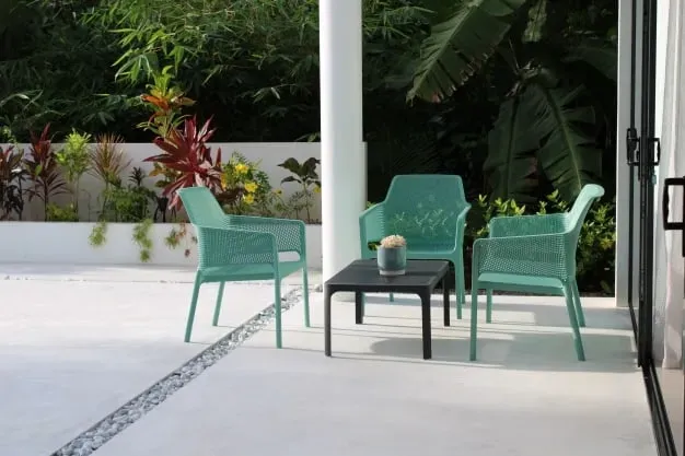 Bright outdoor seating area with turquoise chairs and a black table surrounded by lush tropical plants, perfect for relaxing at Lyla Beach Villa.